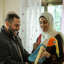 A smiling Imad al-Din al-Saftawi looks at a plush doll held by a smiling young woman