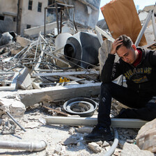 Man holding his head in hand sitting atop rubble