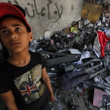 Boy stands in front of room filled with debris