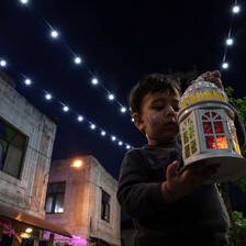 Child holding up a lantern and looking at it. 