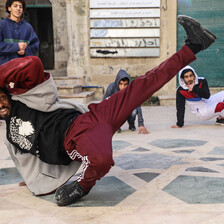 Man makes a breakdance move in front of three onlookers.
