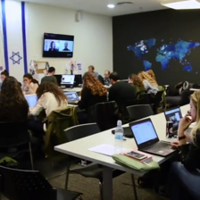 A room full of people working at computers with a large Israeli flag, a world map and monitors on the walls