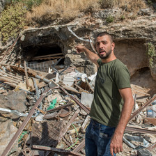 A man points to some rubble behind him