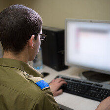 Man in military uniform sits in front of computer