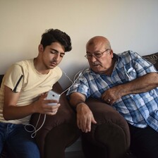 Two men share ear buds as they look at phone