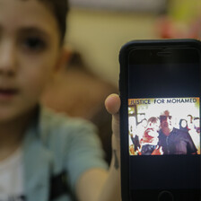 A boy holds a mobile phone with a picture of a man holding a baby