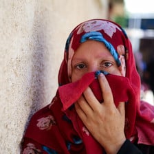 A woman holds a deep red veil up to her face.