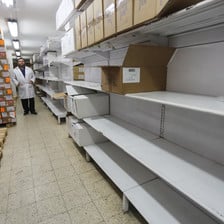 Man stands behind shelves, many of them empty. 