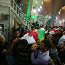 Men carry two dead bodies covered by shrouds and flags. 