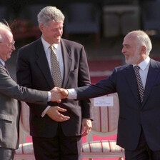 One man watches two others shake hands.