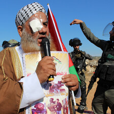 A man with an eyepatch speaks into a microphone while a soldier gesticulates behind him