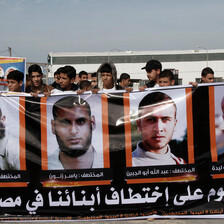 People hold up posters with the pictures of four men. 