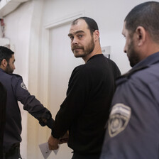 Man walks behind police officer to whom he is handcuffed.