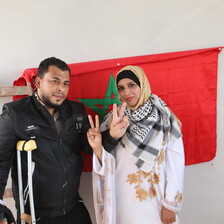 A couple flash the victory sign in front of a Moroccan flag.
