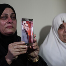 Two women cry, one holds up a picture of a man displayed on a phone