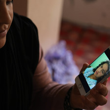 A woman holds a phone showing a picture of herself as a young girl
