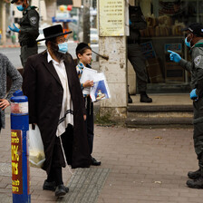 Israeli policeman in face mask gestures at two men in masks and a boy