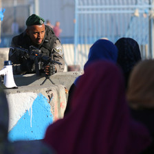 Soldier pointing rifle leans over women at checkpoint