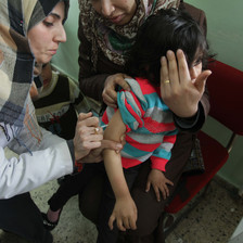 A nurse injects a young child whose face is diverted by her mother