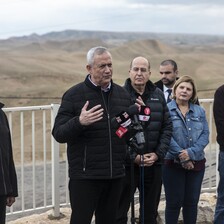 A man talks into several microphones in front of a view of several hills stretching into the distance