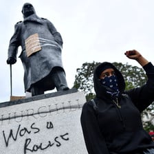Woman stands in front of statue and clenches fist 