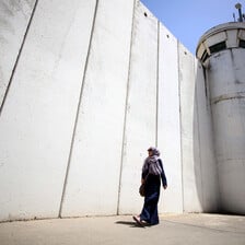 Woman walks past wall and tower 