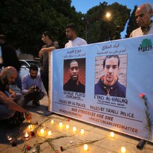 Man lights candles before banner with two portraits of men