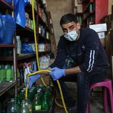 A young man wearing a face mask fills a plastic bottle from a yellow hose