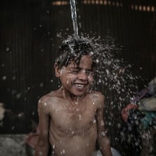 A boy smiles as water is poured over his head