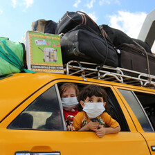 Two children wearing masks look out a car window 