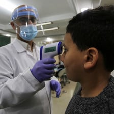 A doctor wearing a face mask is taking a boy's temperature