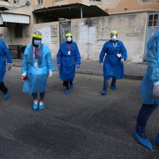 Five nurses in protective gear and masks walk down a street