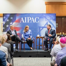 Woman and two men sit on podium with AIPAC sign