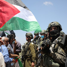 A Palestine flag waves in front of Israeli soldiers