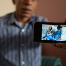 A man holds out a mobile phone showing a still from grainy video footage