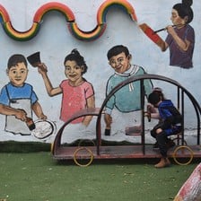 Children play outside in front of a brightly painted wall