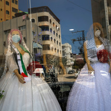 Two mannequins in wedding dresses and face masks are seen through through a shop window