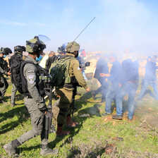 Uniformed soldiers face off against unarmed protestors hidden by a cloud of tear gas