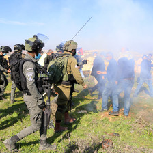 Uniformed soldiers face off against unarmed protestors hidden by a cloud of tear gas