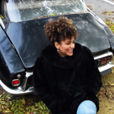 Woman smiles while sitting beside a car 