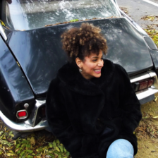 Woman smiles while sitting beside a car