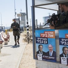 A soldier stands at a concrete checkpoint plastered with posters