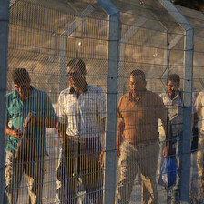 A group of men walk behind a metal fence