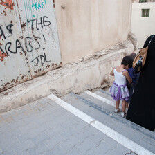 Woman and children walk past wall spray painted with graffiti reading Death to the Arabs!