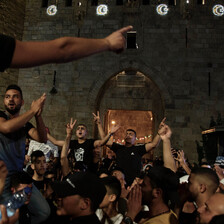 Men carried on shoulders in crowd make victory signs with their hands in front of Old City wall