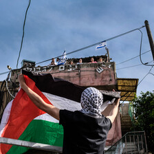 A man holds a flag up as people on top of a building look down