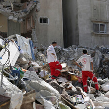 Two health workers stand in the rubble of a destroyed building