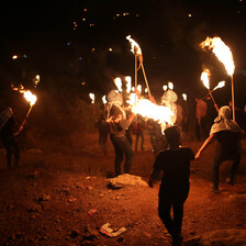 A group of men with lit torches walk across a field in the night