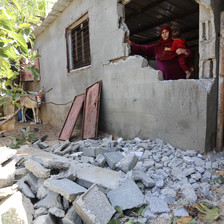 A woman stands behind the remains of a wall of her home