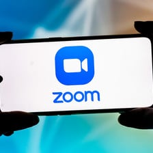 Fingers hold a smartphone displaying Zoom logo